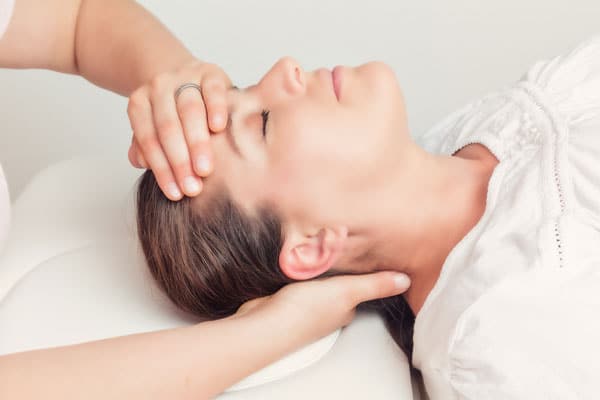 Woman laying on massage table, clinician holding her forehead